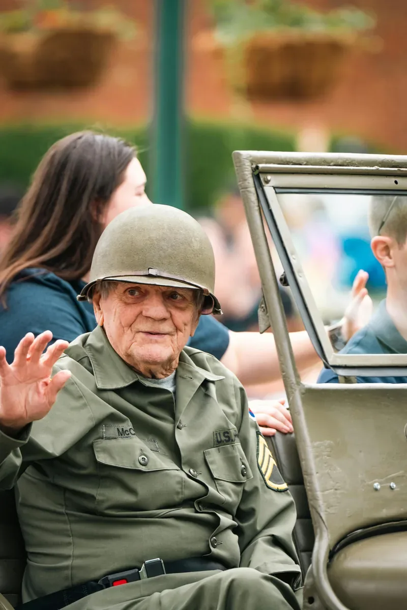 WWII veteran in uniform waving from a jeep